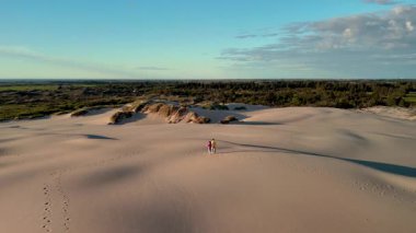 Gün batımı yürüyüşü sırasında Jutlands 'in sakin kumullarının güzelliğini tecrübe edin. İki maceracı, yemyeşil manzaralar ve altın gökyüzü ile çevrili yumuşak arazide dolaşır. Doğa sakinliği gözler önüne seriliyor..