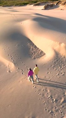 Bir çift, Jutland, Danimarka 'nın pitoresk kum tepelerinde el ele yürür. Güneş batarken yumuşak altın kumda ayak izleri bırakır. Rabjerg Mile kum tepeleri.