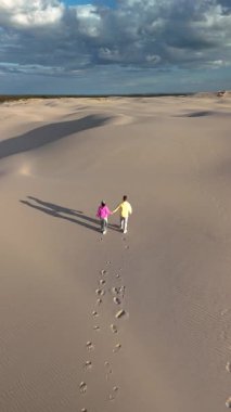 İki birey, Danimarka 'nın Rabjerg Mile Jutland kentindeki çarpıcı kum tepelerinde romantik bir yürüyüşün tadını çıkarıyor. Ayak izleri, dramatik bir gökyüzünün altındaki yumuşak araziyi işaret ediyor.