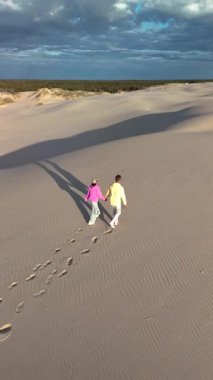 Danimarka, Rabjerg Mile Jutland 'ın sakin kum tepelerinde el ele dolaşırken yumuşak kumda ayak izleri bırakırlar. Altın saat, arazide sıcak bir ışık saçıyor..