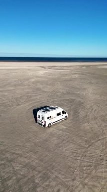 Danimarka 'daki Romo Lakolk Sahili' nin geniş kumlu kıyılarında açık mavi gökyüzünün altında bir karavan duruyor. Huzurlu ortam, rahatlama ve macera arayan yolcuları davet ediyor..