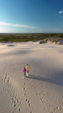 Bir çift Danimarka 'nın Jutland kentindeki sakin kum tepecikli Rabjerg Mil' de huzurlu bir gezintinin tadını çıkarıyor. Açık gökyüzü ve yumuşak kum tepeleri, rahatlama ve bağlantı için mükemmel, sakin bir atmosfer yaratır..