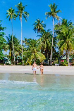 Bir çift, yemyeşil palmiyeler ve kristal berrak sularla çevrili el ele el ele yürür. Sıcak güneş Koh Kood Tayland 'da parlıyor.