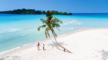 Çiftler, berrak turkuaz sularla çevrili sakin bir plajın el ele tutuşmuş beyaz kumları boyunca el ele yürürler. Bereketli yeşil ada manzaraları Koh Kood 'daki güneşli mavi gökyüzünün altında sakin bir kaçış yaratır.