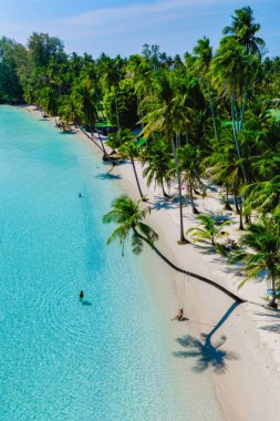 Turkuaz sular, bereketli palmiye ağaçları tarafından çerçevelenmiş el değmemiş beyaz kumlara nazikçe sarılır. Ziyaretçiler, açık bir günde sıcak güneşin tadını çıkaran Koh Kood, Tayland 'ın huzurlu atmosferinin tadını çıkarıyorlar..