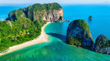 Krabi Tayland 'daki Railay Plajı, berrak mavi gökyüzü altında görkemli kireçtaşı kayalıkları ve canlı yeşilliklerle çevrelenmiş, kıyı nazikçe okşayan turkuaz suları sergiliyor. Rahatlamak için mükemmel..