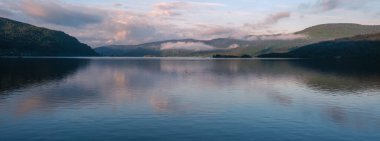 Sakin sular çevredeki dağları yansıtıyor ve şafak vakti bulutlu gökyüzü Norveç fiyortlarında. Güzellik ve sükuneti göstermek için ideal. Araksfjorden Norveç