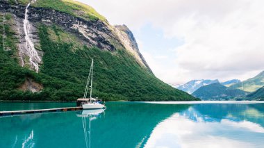 Norveç 'te dingin bir fiyordun nefes kesici manzarası yüksek dağlar ve yemyeşil bitkilerle çevrili. Norangsfjorden 'da sakin bir günde, berrak sulara yansıyan bir yelkenli huzur içinde yanaşır.