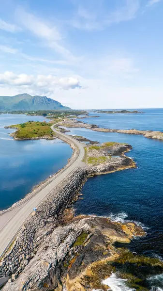 Norveç 'in Atlantik Okyanus Yolu' ndaki sakin mavi sular ve canlı yeşilliklerle çevrili, manzaralı kıyı şeridini kucaklayan muhteşem bir kıyı yolu manzarası.