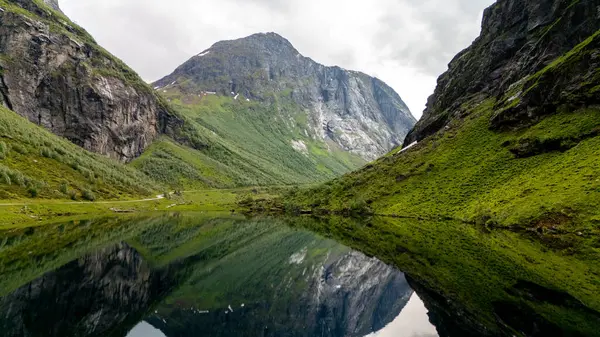 Yüksek dağlar ve sakin sularla Norveç fiyortlarının nefes kesici güzelliğini tecrübe edin. Bereketli yeşillik durgun gölü çevreleyerek, doğanın görkemli manzarasını resmediyor..
