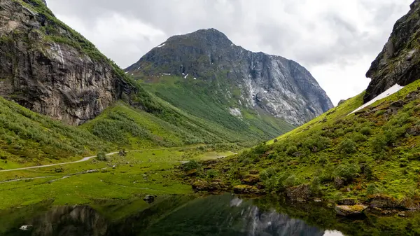 Yeşil yemyeşil tepeler ve yüksek dağlar, Norveç 'in yaz aylarındaki dramatik manzarasını yansıtan sakin bir su kütlesinin etrafını sarar. Doğa güzelliği keşfi davet eder.