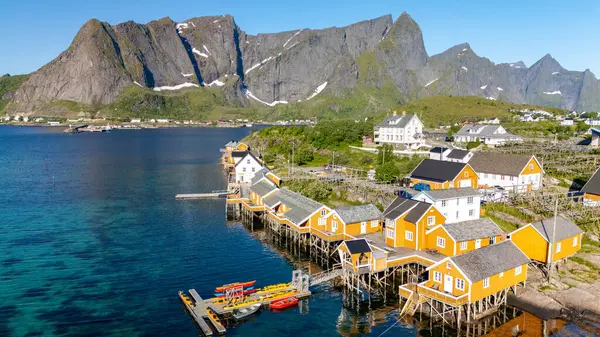 Parlak sarı kulübeler Norveç fiyortlarının dingin sularını kaplar. Arka planda görkemli dağlar yükselir, doğa ve mimarinin mükemmel bir karışımını yaratır. Lofoten Norveç