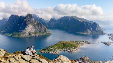 İki yürüyüşçü, açık güneşli bir günde Norveç 'teki nefes kesen Lofoten Adaları' na bakan kayalık bir çıkıntıda dinleniyor. Reinebringen dağı Lofoten Norveç 'te yürüyüş yapan çift