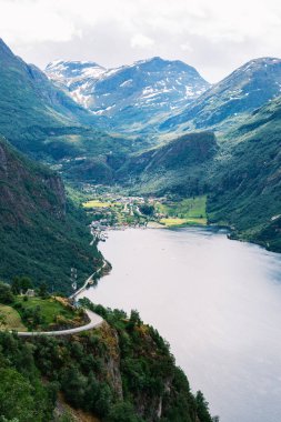 Norveç 'in dağlık arazisinin büyüleyici güzelliğini keşfedin. Sakin bir fiyordun üzerindeki uçurumları saran dolambaçlı bir yol. Yeşillik ve canlı vadiler güzel bir ortam yaratıyor. Geiranger fiyordu