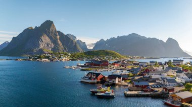 Reine Lofoten Norveç 'teki nefes kesici kıyı köyünde berrak mavi gökyüzünün altında renkli ahşap evler, dingin sular ve görkemli dağ zirveleri sergileniyor..