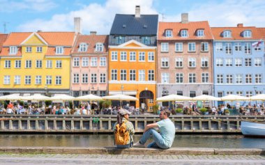 Nyhavn, Kopenhag, Danimarka. Parlak renkli binalar, yerel halkın ve ziyaretçilerin açık kafelerde dinlendiği rıhtımda yer alıyor. Sıcak, güneşli bir gün bu büyüleyici kasabadaki hayat dolu atmosferi güçlendirir..