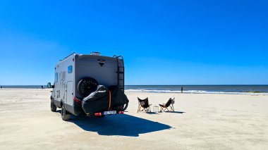 Romo Danimarka 12 Mayıs 2025, kumlu bir plaja park etmiş modern bir karavan rahatlamak için mükemmel bir yer sağlıyor. İki sandalye sakin denize bakıyor ve sahile gidenler için davetkar bir atmosfer yaratıyor..