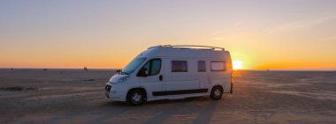 Güneş batarken sakin bir plajda duran bir karavan gökyüzünde sıcak renkler bırakıyor. Bu huzurlu an, Danimarka 'nın doğal güzelliklerindeki macera ve rahatlama ruhunu yakalar..