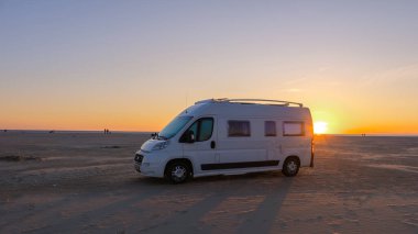 Danimarka 'da sakin bir kumlu plajda gün batımında park etmiş beyaz bir karavan. Lakolk Strand, Romo Danimarka