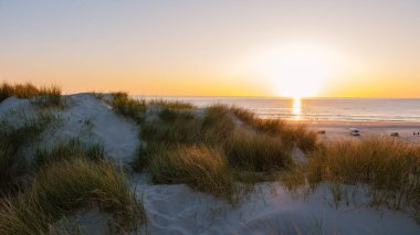 Altın renkler, güneş ufuktan yükselirken Danimarka 'nın sakin plajını aydınlatıyor. Dalgalar yavaşça kıyıya çarpar ve bu kıyı kaçışının sakin atmosferini güçlendirir..