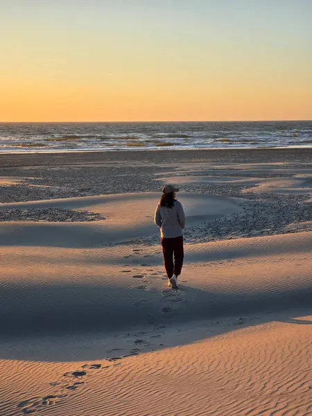 Günbatımında Danimarka 'da bir sahil sahilinin yumuşak kumlarında tek başına gezinen bir figür. Turuncu ve pembe renkli dalgalar yavaşça kıyıya vururken gökyüzünü dolduruyor..