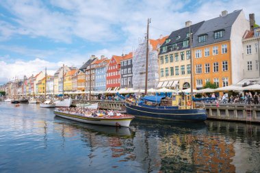 Nyhavn, Kopenhag, Danimarka, 12 Temmuz 204: Turistler tekne gezintilerinden ve yerel halk açık havada yemekten hoşlanıyor. Çarpıcı derecede renkli cepheler berrak mavi gökyüzünün altındaki sakin suları yansıtıyor..
