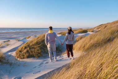 Danimarka kıyısındaki altın kum tepelerinde el ele gezen bir çift. Uzun otlar ve nefes kesici okyanus manzaralarıyla çevrili. Blokhus Strand, Danimarka