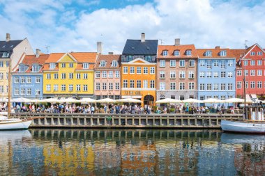 Nyhavn, Kopenhag, Danimarka, 12 Temmuz 204: Yerel halk ve ziyaretçiler kafelerde toplanırken sakin sularda yansıyan, deniz kıyısında parlak boyanmış binalar. 