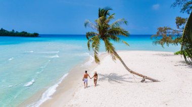 Bir çift, tropikal bir plajda romantik bir yürüyüş, ayak altında sıcak kumlar ve ufukta uzanan turkuaz suların keyfini çıkarıyor. Koh Kood Tayland adasında tatilde olan çift.