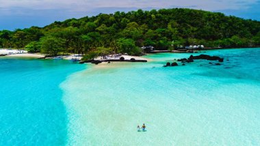 Çift, turkuaz sularla çevrili güzel bir sahil boyunca romantik bir gezinti yapar ve berrak bir gökyüzünün altında yemyeşil bir yer. Koh Mak Tayland yakınlarındaki Koh Kham Adası.