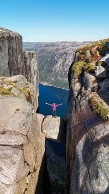 Bir maceracının göz kamaştırıcı manzarayı kucakladığı, Lysefjord, Norveç 'in yukarısında canlı bir an. Kjeragbolten Lysefjord, Norveç