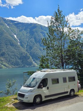 Norveç 'te sakin bir fiyordun yanına park etmiş bir karavan, açık mavi gökyüzünün altında görkemli dağlarla çevrili. Doğada macera arayan gezginler için mükemmel güzellik..