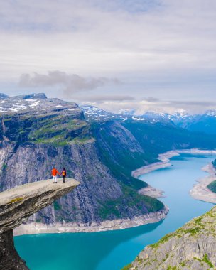 Yürüyüşçüler Norveç, Trolltunga 'nın kıyısında duruyor, aşağıdaki muhteşem fiyorda hayret ediyorlar. Görkemli uçurumlar sakin sulardan keskin bir şekilde yükselir ve Norveç 'in doğal güzelliklerini yakalar..