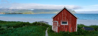 Lofoten Norveç 'te kumlu bir plajın yanında, yemyeşil ve arka planda dağlarla çevrili tuhaf kırmızı bir kulübe bulunur. Huzurlu kıyı manzarası doğaya ve sükunete mükemmel bir kaçış sunuyor..