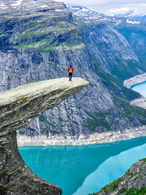 Norveç 'te dramatik bir uçurumun kenarında duran yalnız bir maceracı aşağıdaki parıldayan turkuaz fiyorda bakıyor. Trolltunga yürüyüşü Norveç