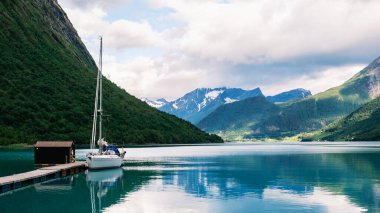 Sakin sular, bir yelkenlinin iskeleye yanaşması gibi Norveç 'in çarpıcı manzarasını yansıtıyor. Yeşil yemyeşil tepeler ve yüksek dağlar Norangsfjorden Norveç 'in sakin fiyortlarını çevreledi.