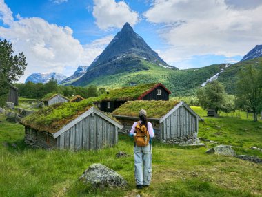 Bir gezgin Norveç 'in bereketli yeşil manzarasını keşfeder, manzaralı dağlar ve çimen çatılı geleneksel ahşap kulübelerle çevrilidir. Doğa ve kültürün mükemmel bir karışımı..