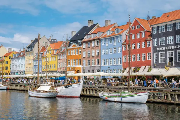Nyhavn, Kopenhag, Danimarka, 12 Temmuz 204: Renkli tarihi binalar Norveç 'in canlı bir kasabasında rıhtımda yer alıyor. İnsanlar açık kafelerde toplanırken yelkenliler limanda usulca sallanıyor.