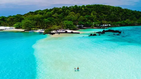 Çift, turkuaz sularla çevrili güzel bir sahil boyunca romantik bir gezinti yapar ve berrak bir gökyüzünün altında yemyeşil bir yer. Koh Mak Tayland yakınlarındaki Koh Kham Adası.
