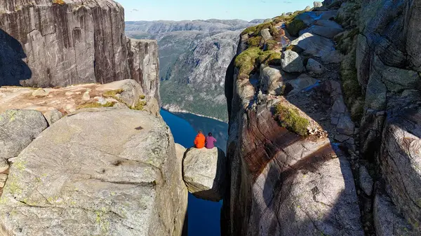 Ziyaretçiler bir uçurumun kenarındaki dramatik bir kaya oluşumunda oturup fiyortun derin mavi sularına bakarak görkemli dağlarla çevrili. Kjeragbolten Lysefjord, Norveç