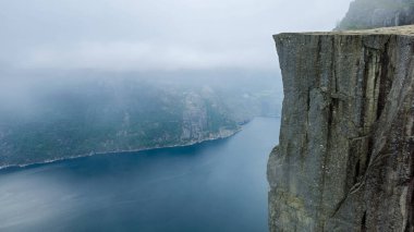 Lysefjord Preikestolen, Norveç 'in baş döndürücü güzelliğini deneyimleyin. Yüksek uçurumların sakin sularla buluştuğu yer. Sis, bu İskandinav cennetinin huzurlu atmosferini yükselterek araziyi kaplıyor..