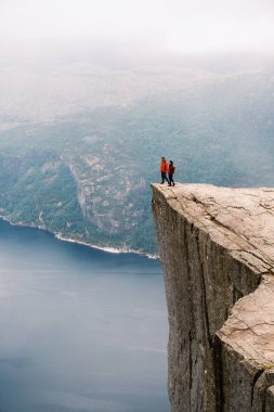 Norveç 'teki Preikestolen uçurumunun kenarında duran iki maceraperest yürüyüşçü çevredeki fiyortların nefes kesici manzarasını seyrediyor. Sisli atmosfer doğanın cazibesine güzellik katar..