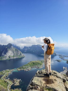 Bir yürüyüşçü Norveç 'teki büyüleyici Lofoten Adalarına bakan kayalık bir çıkıntıda duruyor. Görkemli dağlar ve derin mavi sular resim gibi bir manzara yaratır..