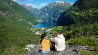 Bir çift Norveç 'teki Geirangerfjord' a bakan kayalık bir çıkıntıda rahatlıyor. Yeşillik ve dik dağlarla çevrili manzara, Norveç doğasının özünü yakalıyor..