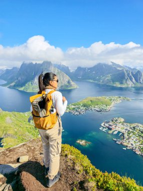 Sırt çantası takan bir yürüyüşçü, Norveç 'teki Lofoten Adaları boyunca dramatik dağlar ve sakin sularla çevrili bir şekilde dik dik bakar. Bu çarpıcı manzara bölgenin doğal güzelliğini gözler önüne seriyor..