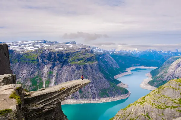 Yalnız bir yürüyüşçü, Trolltunga 'nın dramatik uçurumunda durur. Etrafı görkemli dağlarla ve aşağıdaki turkuaz gölle çevrilidir. Sakin atmosfer, Norveç 'in vahşi doğasının güzelliğini yansıtıyor..