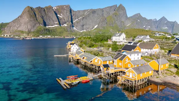 Canlı sarı balıkçı kulübeleri, muhteşem İskandinav manzarasını yansıtan Reine, Lofoten Adaları 'nın sakin rıhtım hattını oluşturur..