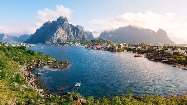 Norveç 'te sakin bir fiyordun üzerinde heybetli dağlar yükseliyor ve kıyı şeridi boyunca uzanan tuhaf balıkçı kulübeleri var. Reine Lofoten Norveç