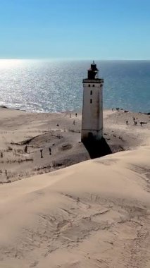 Geniş kum tepeleri, Kuzey Denizi 'nin Rubjerg Knude Fyr Deniz Feneri' ndeki köpüklü sularına çıkar. Danimarka 'nın Jutland şehrinde mavi gökyüzüne bakan yükselen beyaz bir deniz feneri var.