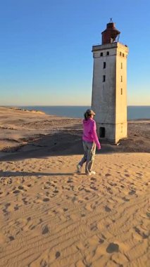 Danimarka 'nın Rubjerg Knude Jutland kıyı şeridi boyunca yürüyen bir figür olarak pürüzsüz kumda ayak izleri var. Deniz feneri gün batımına karşı dimdik ayakta duruyor.